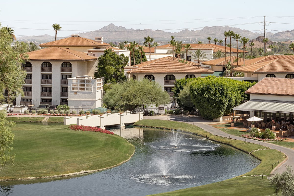 A resort with a pool, palm trees, and a mountainous backdrop.