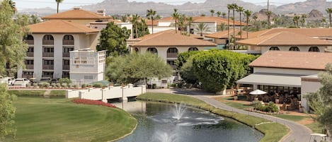 A resort with a pool, palm trees, and a mountainous backdrop.