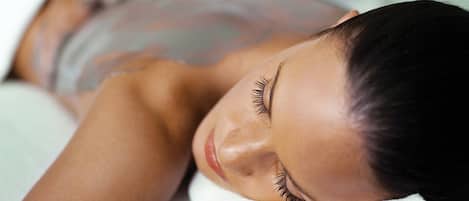 A person lying on a bed with a white cover, suggesting a spa or relaxation setting.