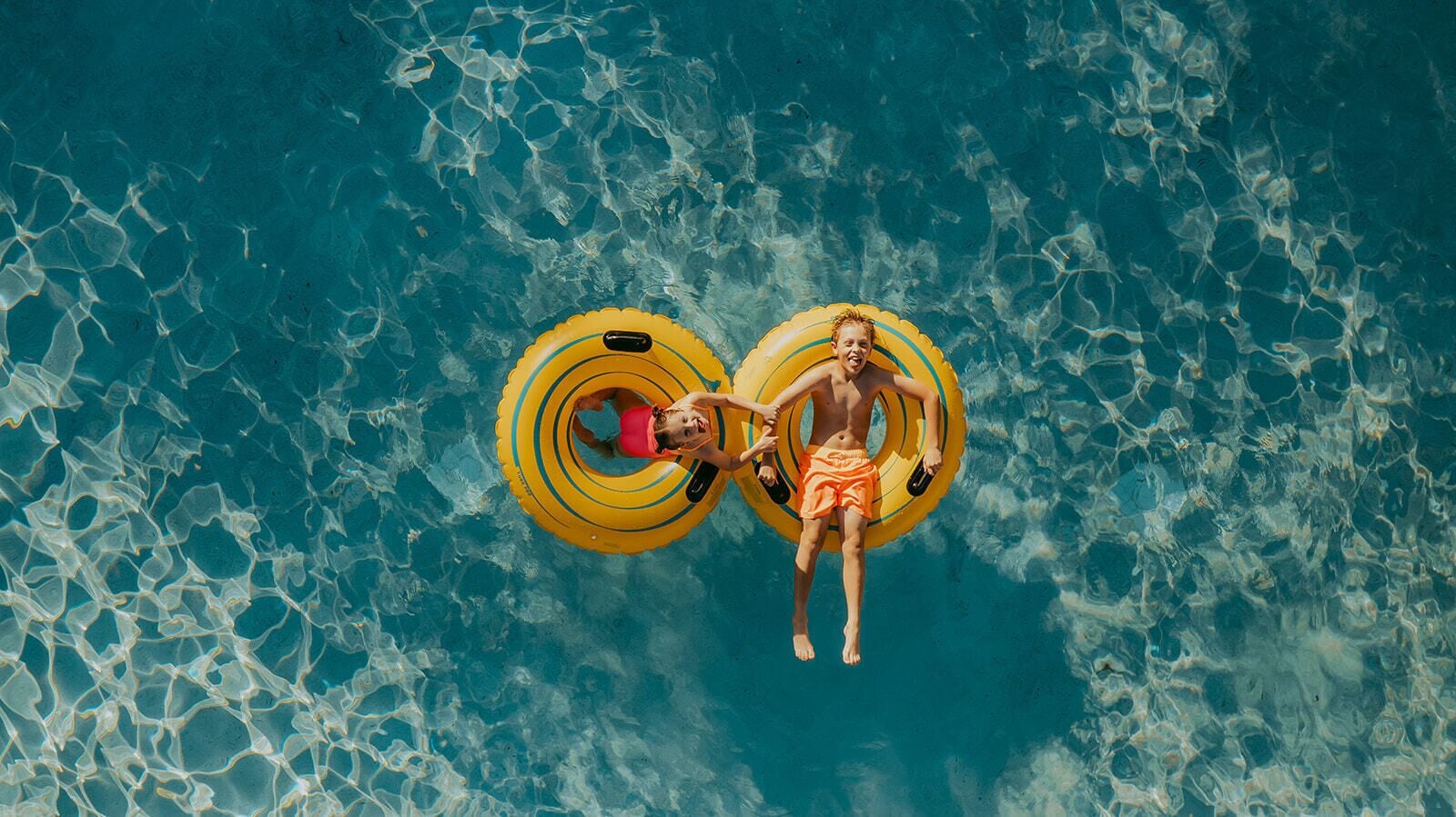 An aerial view of a swimming pool with two people floating on yellow inflatable rings.