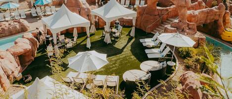 A poolside area with white canopies, lounge chairs, and a rocky landscape.