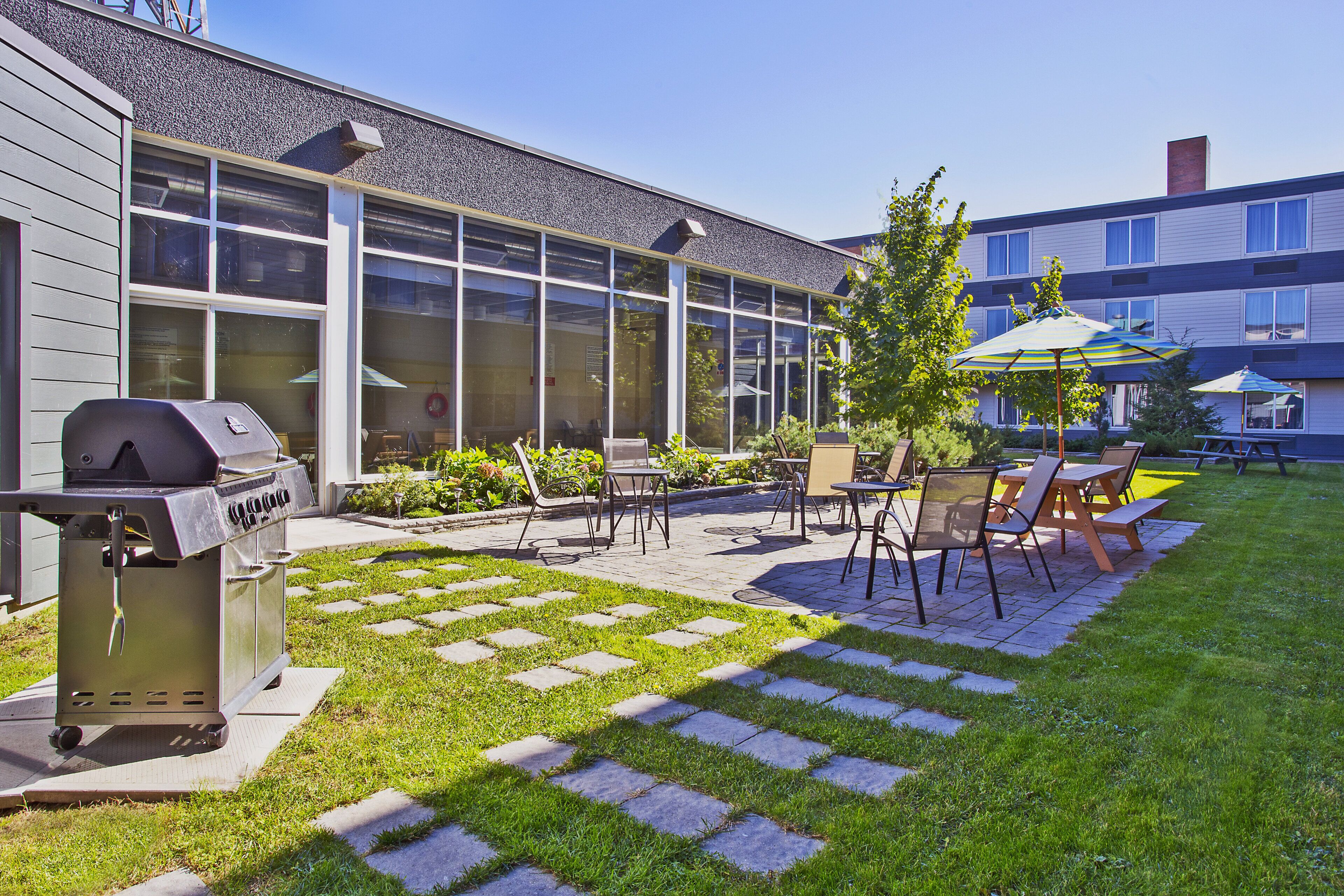 An outdoor patio area with a grill, seating, and a view of a building with large windows.
