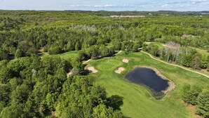 An aerial view of a golf course surrounded by dense forest, with a pond and sand bunkers. - Holiday Inn Express Sault Ste Marie by IHG (Sault Ste. Marie)