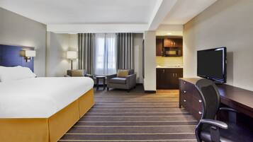 Une chambre d’hôtel comprenant un grand lit, un bureau avec une chaise, une télévision, une petite table avec une chaise et un coin cuisine.