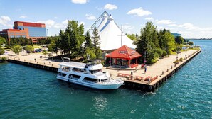 A waterfront area with a dock, a white boat, a red-roofed pavilion, and a large building in the background. - Holiday Inn Express Sault Ste Marie by IHG (Sault Ste. Marie)