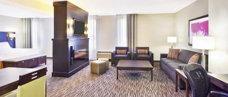A hotel room with a flat-screen TV, a sofa, a coffee table, a desk, and a chair.