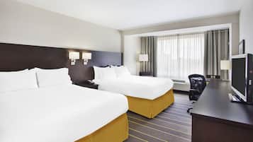 Quarto de hotel com duas camas, uma escrivaninha, televisão e janela com cortinas.