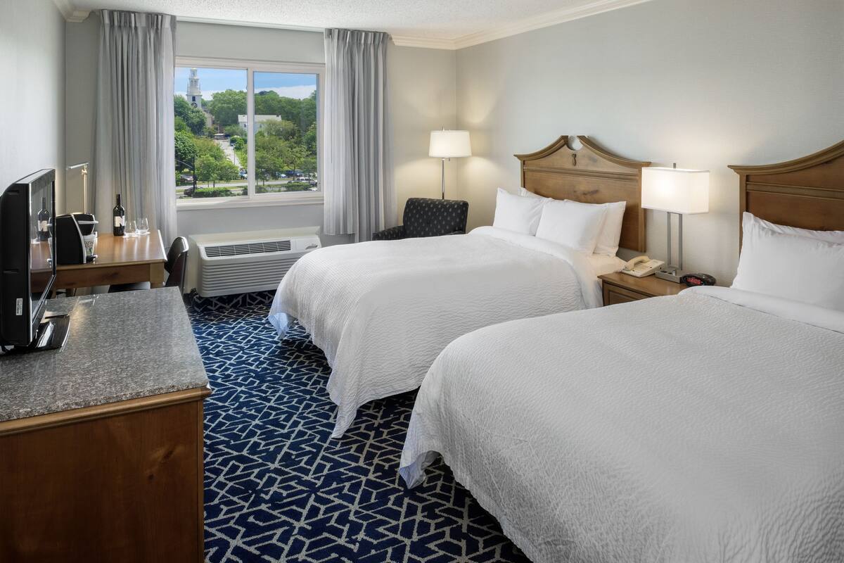 A hotel room with two beds, a desk with a computer, a chair, and a window with curtains.