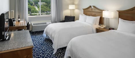 A hotel room with two beds, a desk with a computer, a chair, and a window with curtains.