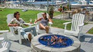 Two people seated at a table with a fire pit in the center, surrounded by white Adirondack chairs, with a marina and boats in the background. - The Newport Harbor Hotel & Marina (Newport)