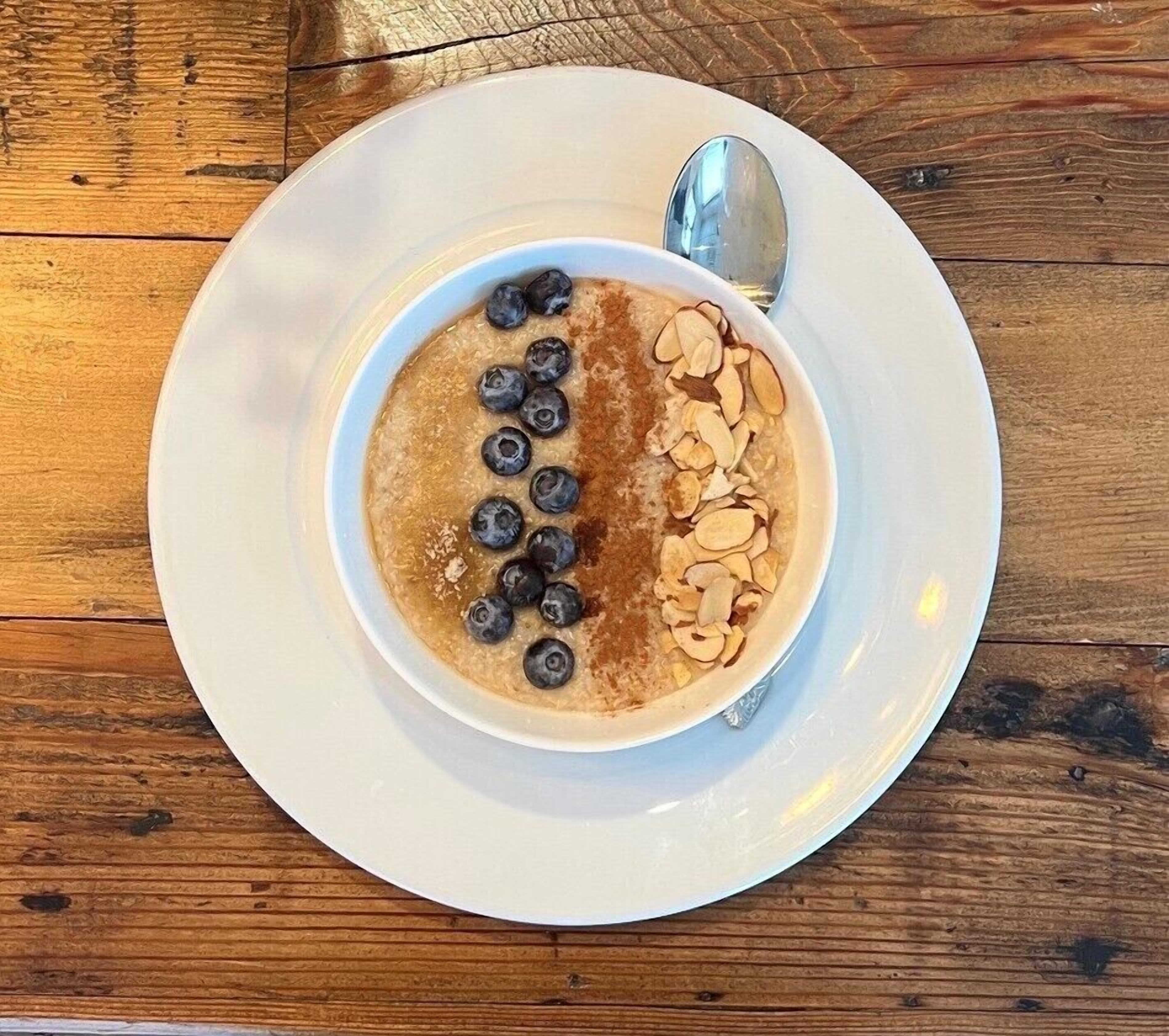 A bowl of oatmeal topped with blueberries and sliced almonds on a white plate, with a spoon beside it.