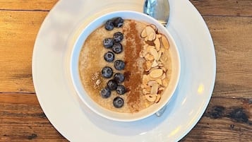 A bowl of oatmeal topped with blueberries and sliced almonds on a white plate, with a spoon beside it.