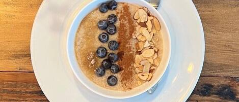 A bowl of oatmeal topped with blueberries and sliced almonds on a white plate, with a spoon beside it.