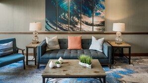 A modern lobby with a grey sofa, two side tables with lamps, a coffee table with decorative items, and a large wave-themed painting on the wall. - The Newport Harbor Hotel & Marina (Newport)
