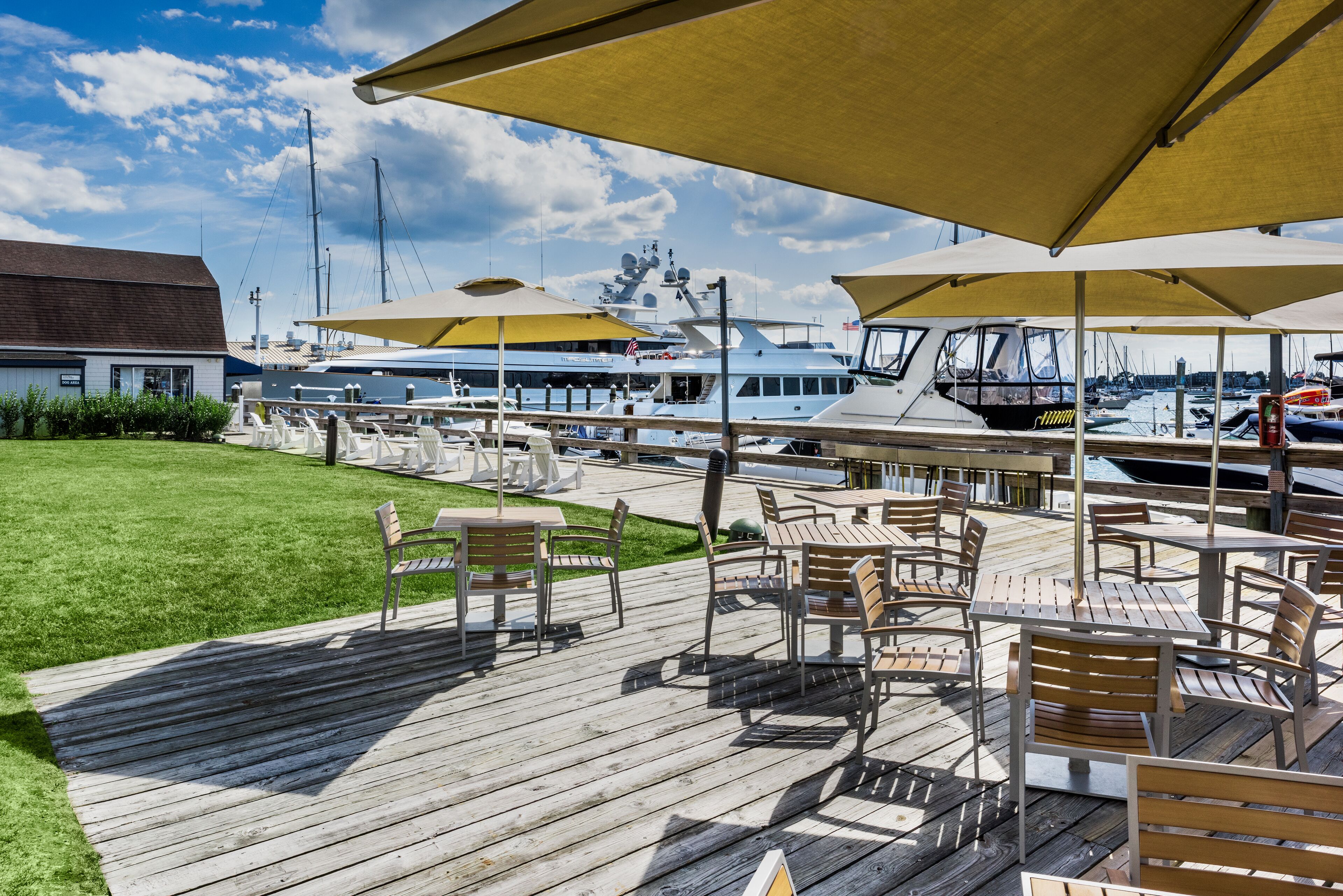 A wooden deck with outdoor seating and umbrellas, overlooking a marina with boats.