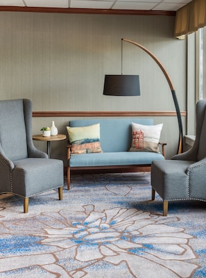 A room with a blue sofa, two grey armchairs, a small round table with a plant, and a patterned carpet.