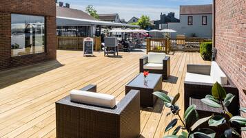 A wooden deck with wicker furniture, a table with a vase, and a signboard.