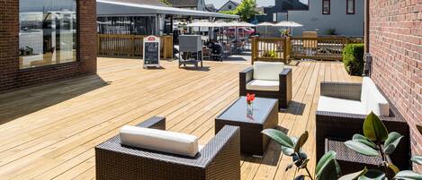 A wooden deck with wicker furniture, a table with a vase, and a signboard.