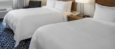 A hotel room with two beds, a nightstand with a phone and alarm clock, a chair, and a view of the outdoors.