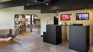 A modern reception area with a wooden counter, seating, and a TV screen displaying information.