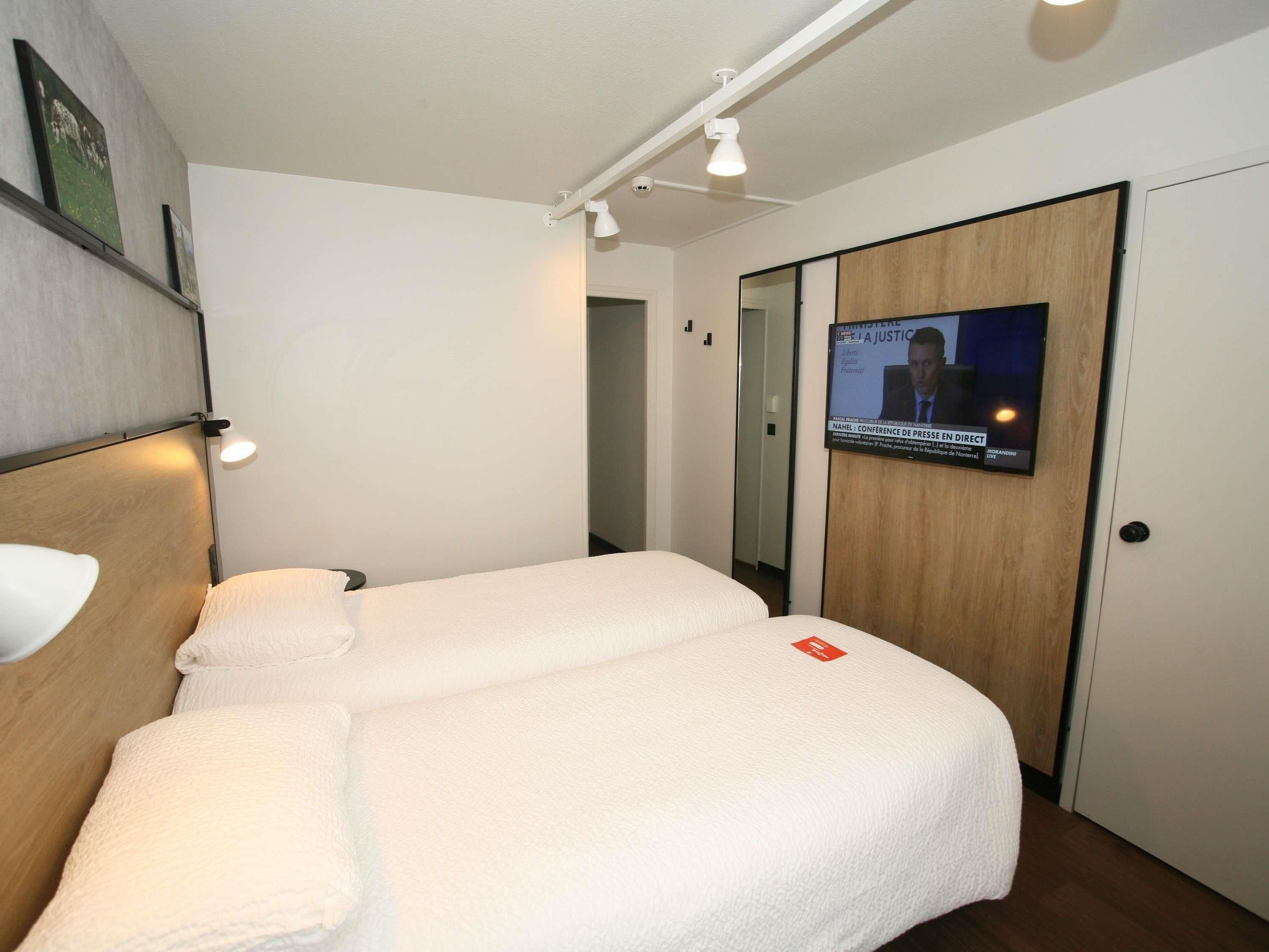 Ein Hotelzimmer mit einem Bett, einem an der Wand montierten Fernseher und einer Tür mit Holzpaneel.