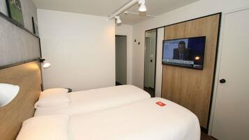 Ein Hotelzimmer mit einem Bett, einem an der Wand montierten Fernseher und einer Tür mit Holzpaneel.