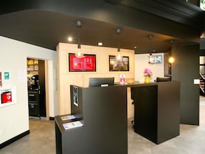 A reception area with a wooden counter, two monitors, and a coffee machine. - ibis Saint Lo La Chevalerie (Saint-Lo)