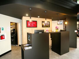 A reception area with a wooden counter, two monitors, and a coffee machine.