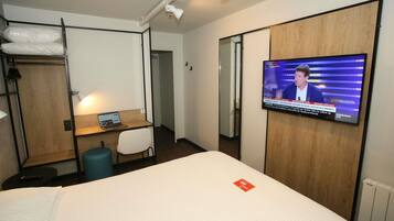 A hotel room with a bed, a desk with a laptop, a TV on the wall, and a wardrobe.