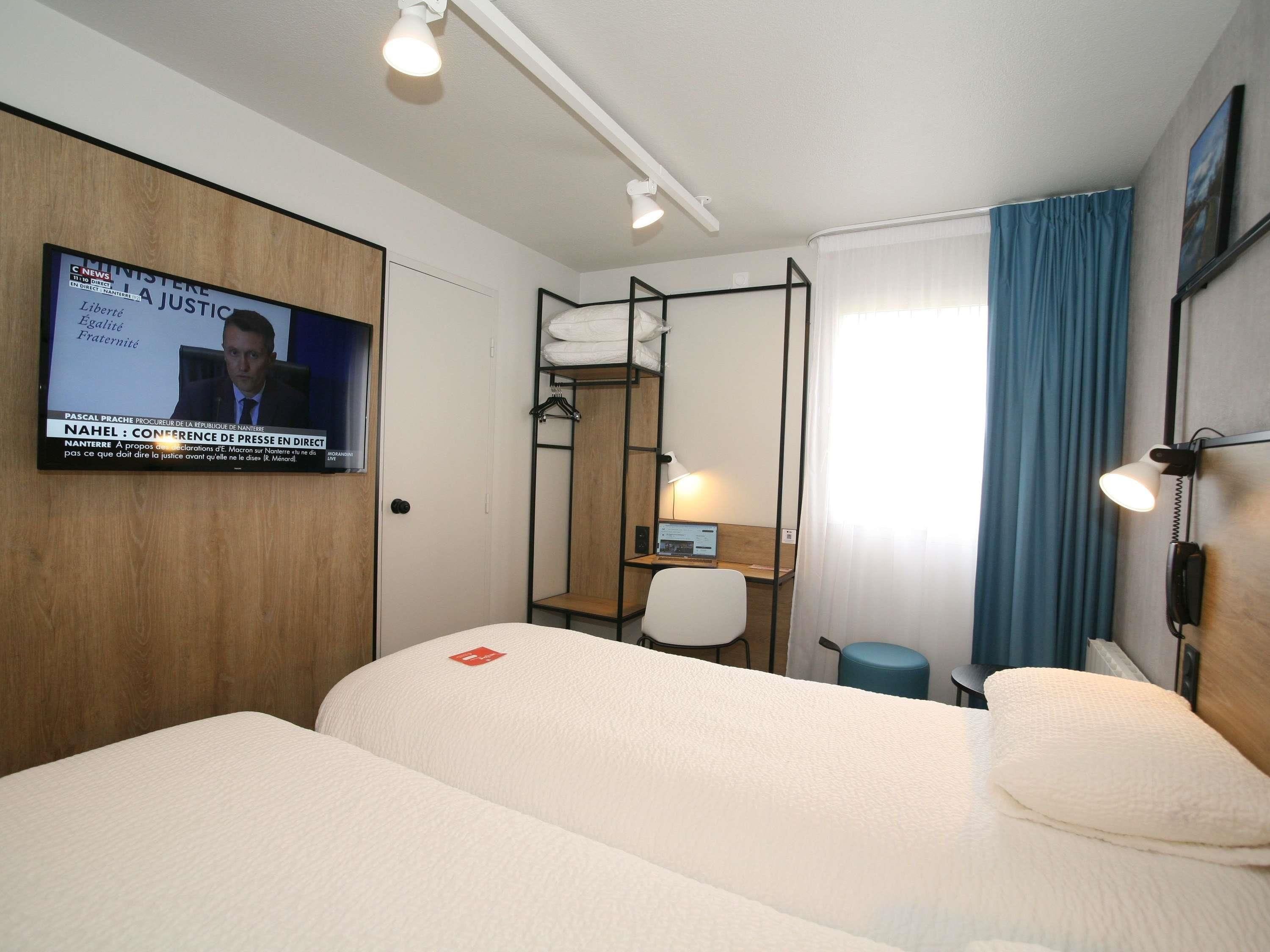 Habitación de hotel con dos camas, un escritorio, una silla, un televisor montado en la pared y un teléfono.