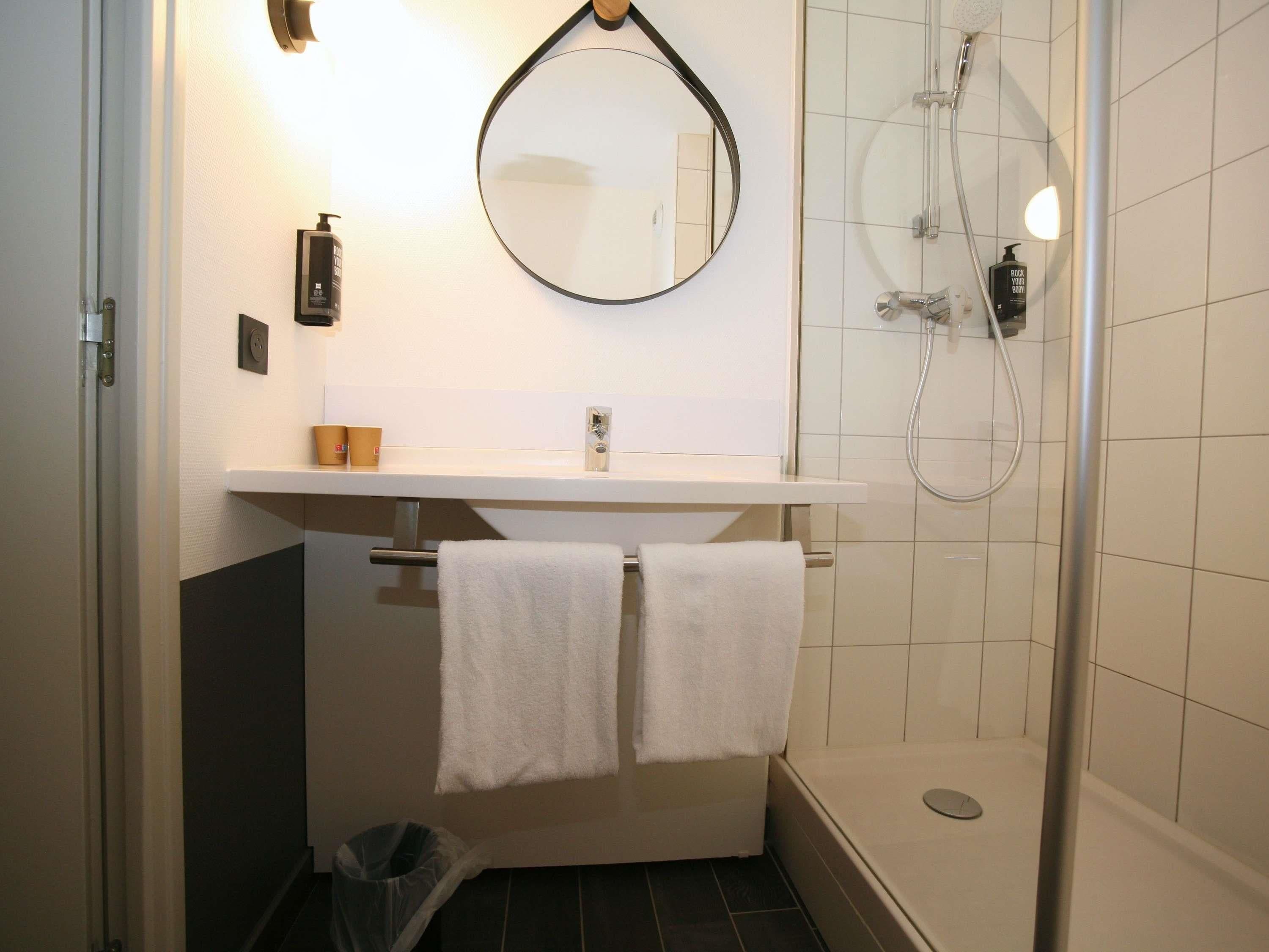 Un baño con ducha, lavabo, espejo y dos toallas colgadas en un perchero.