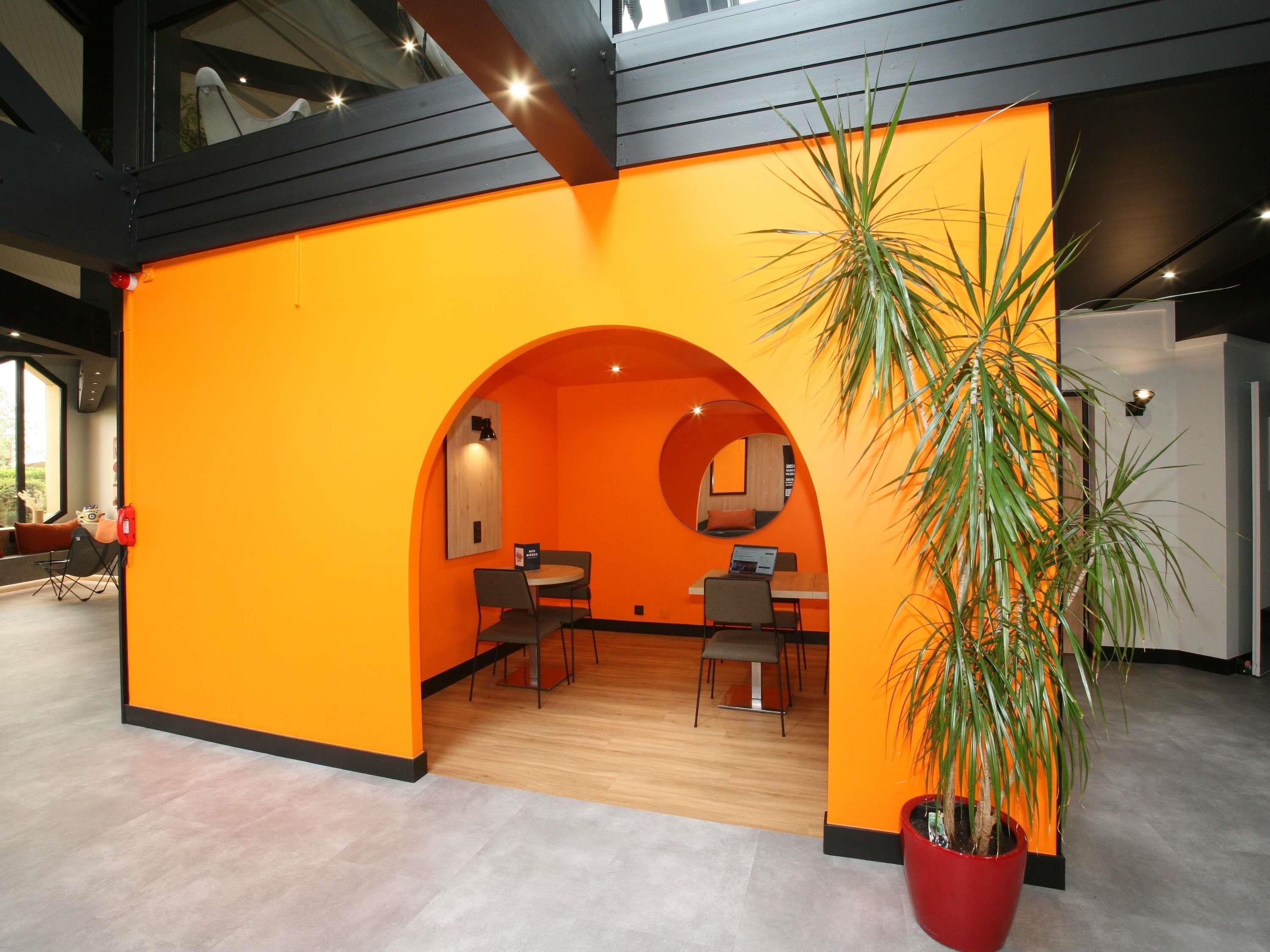 A modern interior with an orange accent wall, a round mirror, and a potted plant.