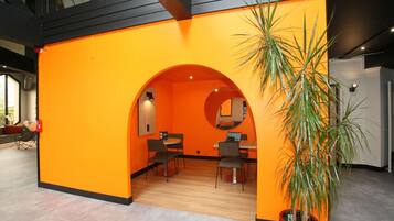 A modern interior with an orange accent wall, a round mirror, and a potted plant.
