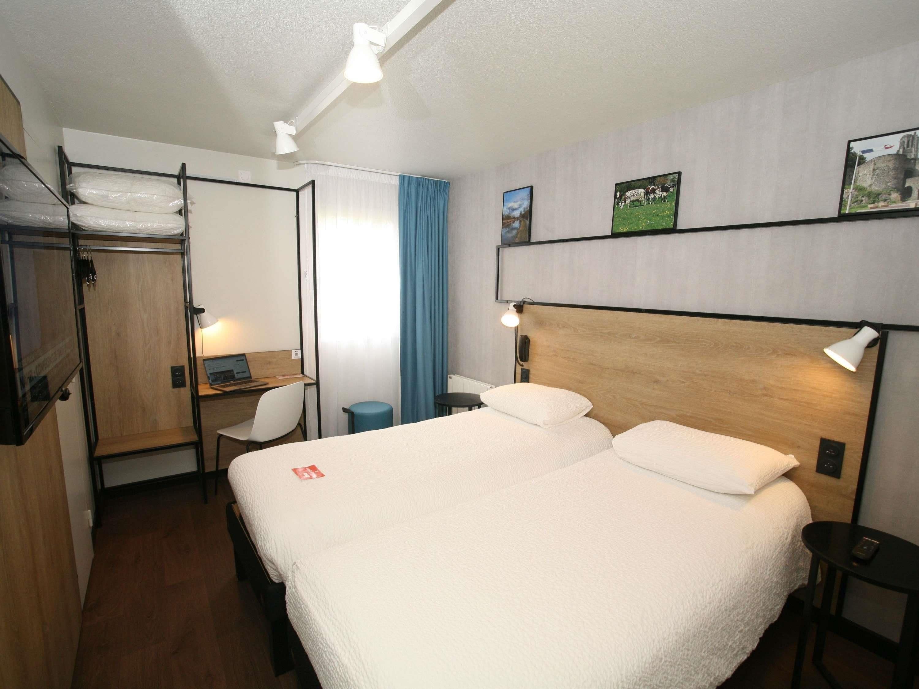 A hotel room with a bed, desk, chair, and a wardrobe.