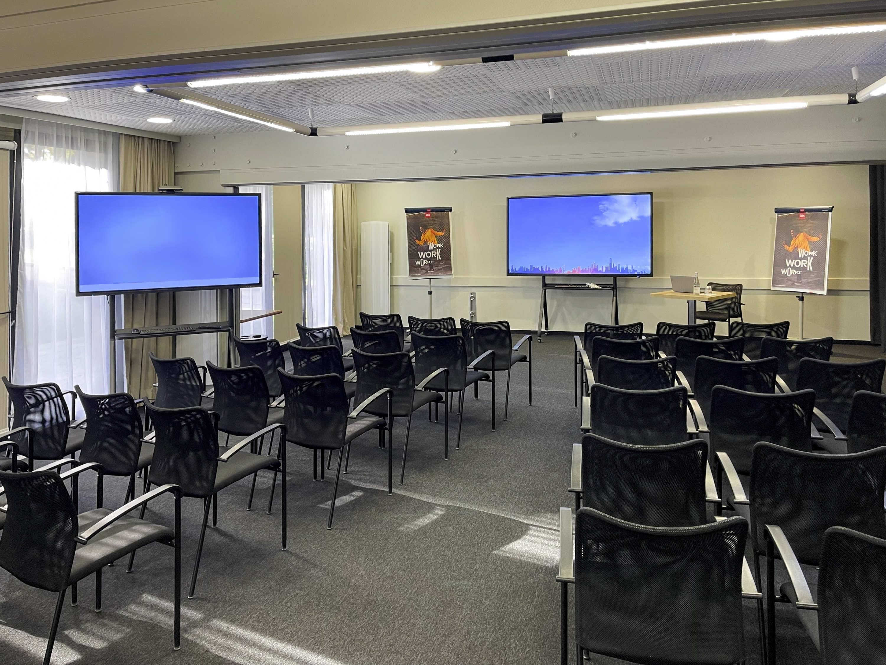 A conference room with rows of chairs, two large screens, and banners on the walls.