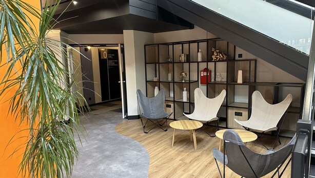 A modern interior with a curved wooden floor, a potted plant, and a staircase leading to a mezzanine.