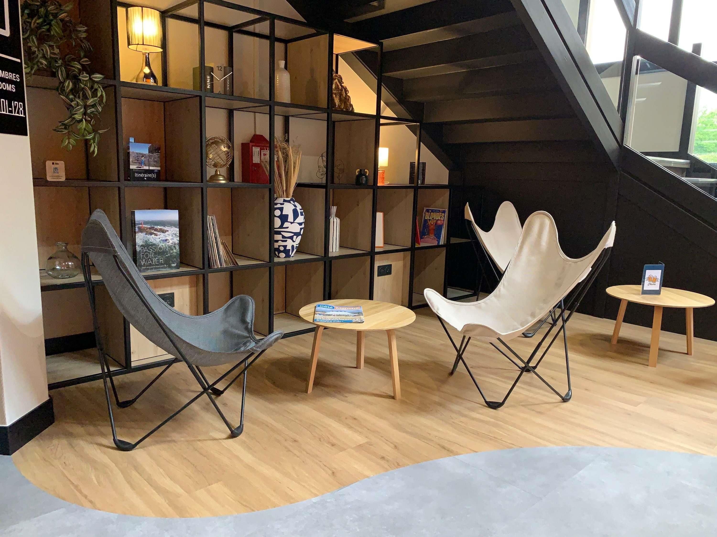 A modern interior with a bookshelf, two chairs, a small table, and a staircase.
