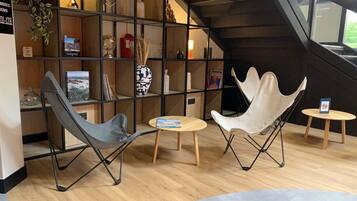 A modern interior with a bookshelf, two chairs, a small table, and a staircase.