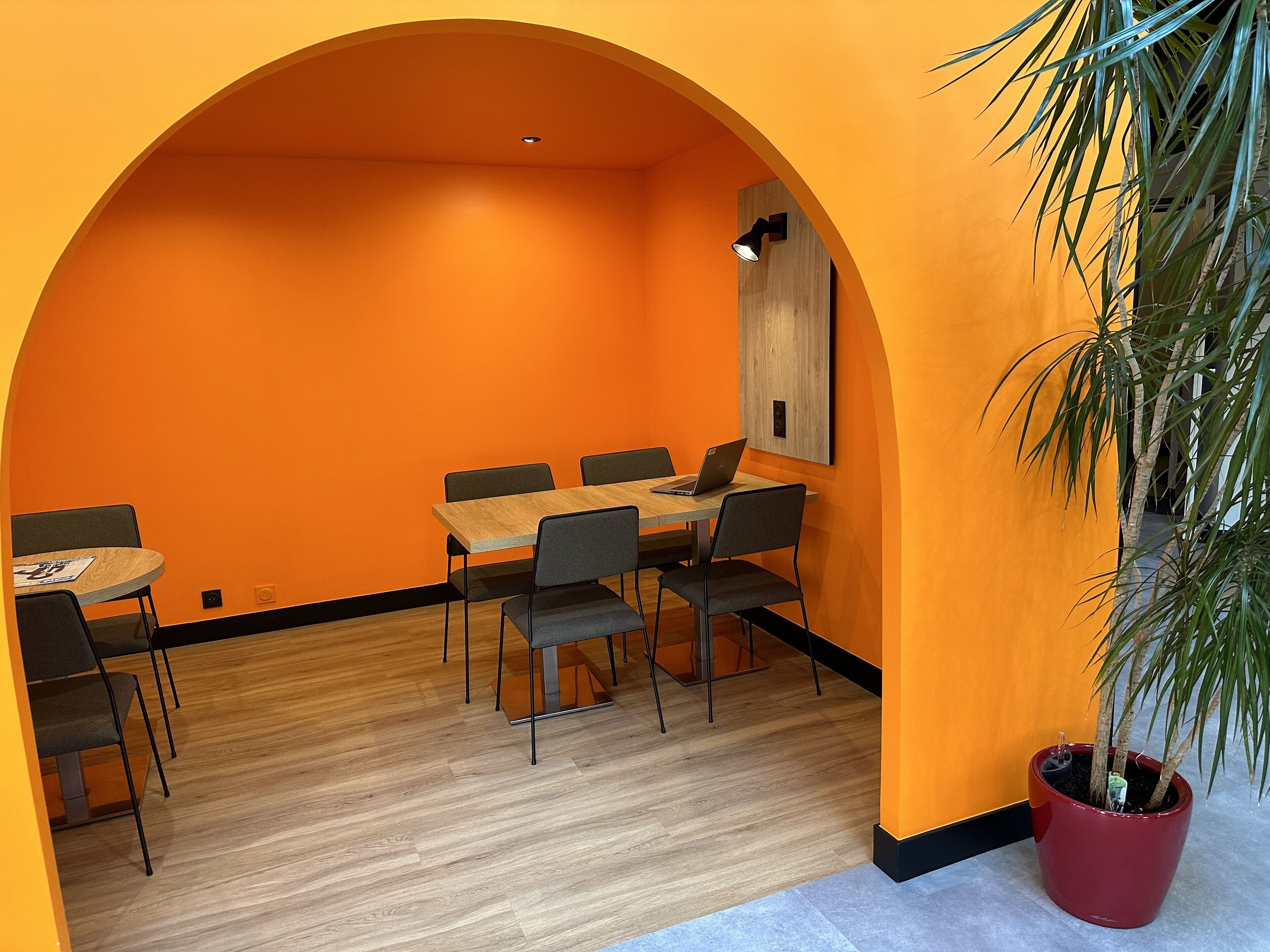Una sala de conferencias con una mesa de madera, cuatro sillas, una planta en maceta y una lámpara fijada a la pared.