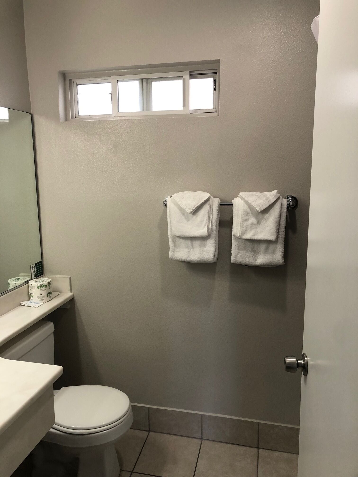 Un baño con inodoro, lavamanos y dos toallas colgadas en un perchero.