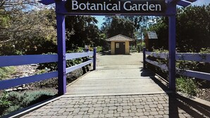 Un percorso conduce all'ingresso del Giardino Botanico, con un pergolato sopra e un piccolo edificio sullo sfondo.