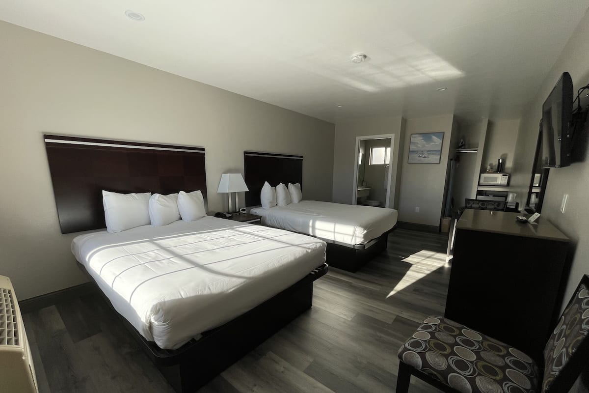 A hotel room with two beds, a desk, a chair, and a bathroom visible through an open door.