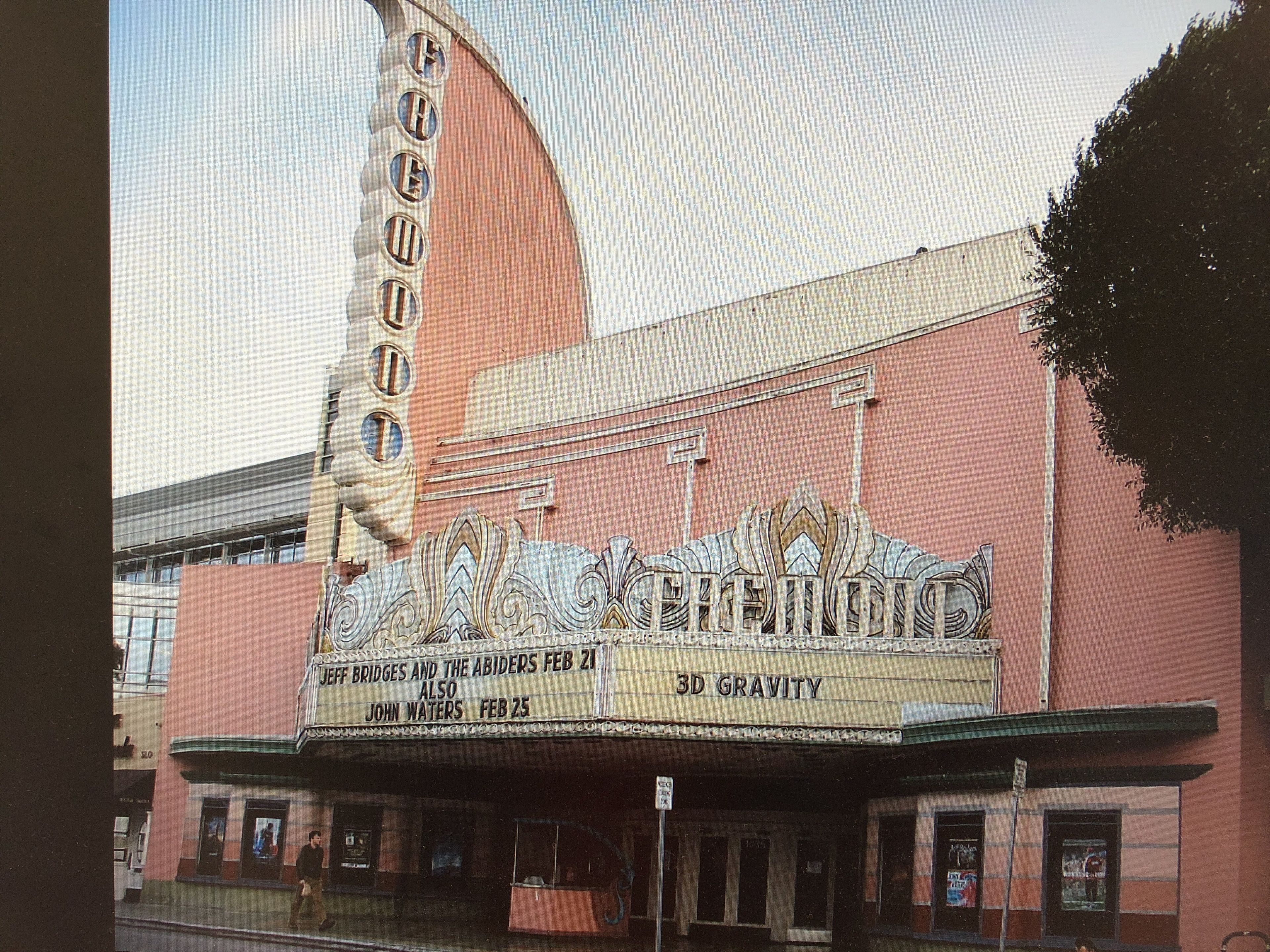 A theater with a curved marquee displaying movie titles and dates.