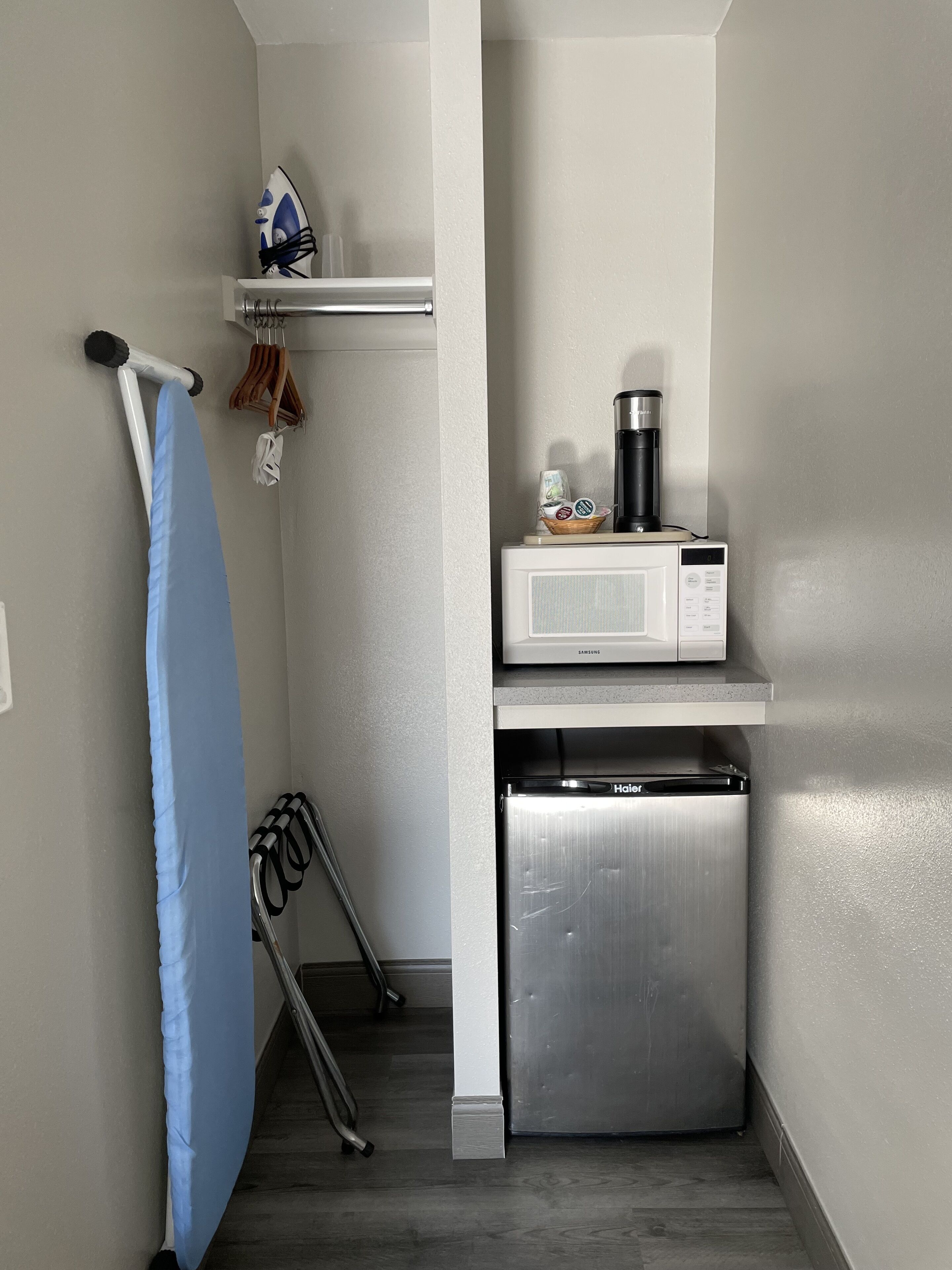 A compact kitchen with a microwave, refrigerator, and ironing board.