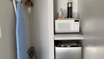A compact kitchen with a microwave, refrigerator, and ironing board.