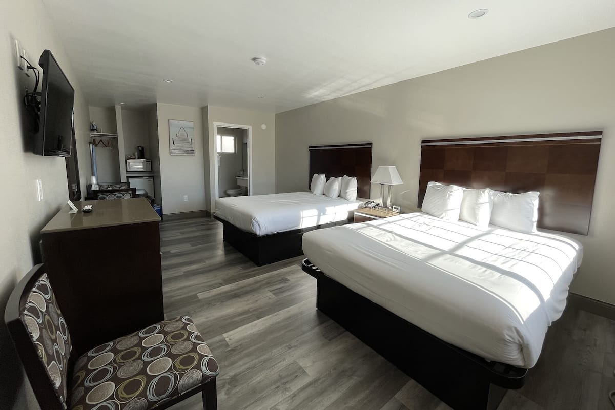 A hotel room with two beds, a desk, a chair, and a television.