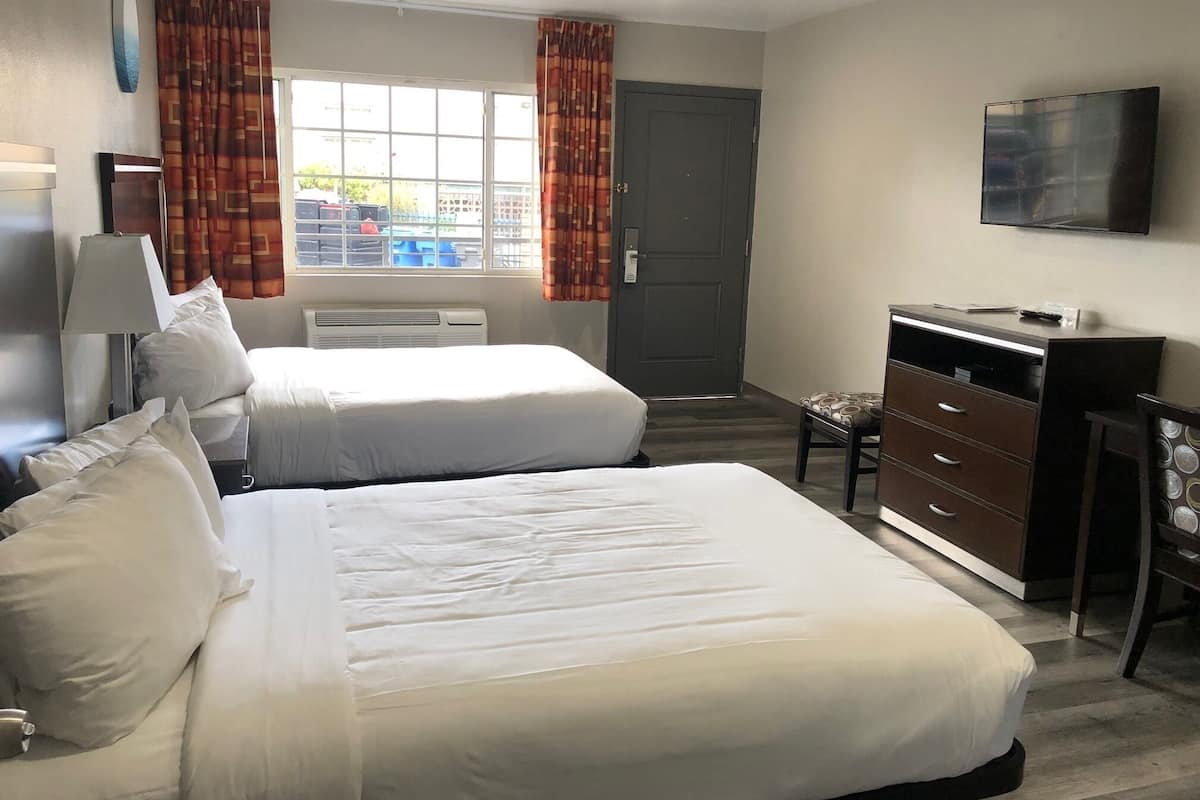 A hotel room with two beds, a desk, a chair, a TV, and a window with curtains.