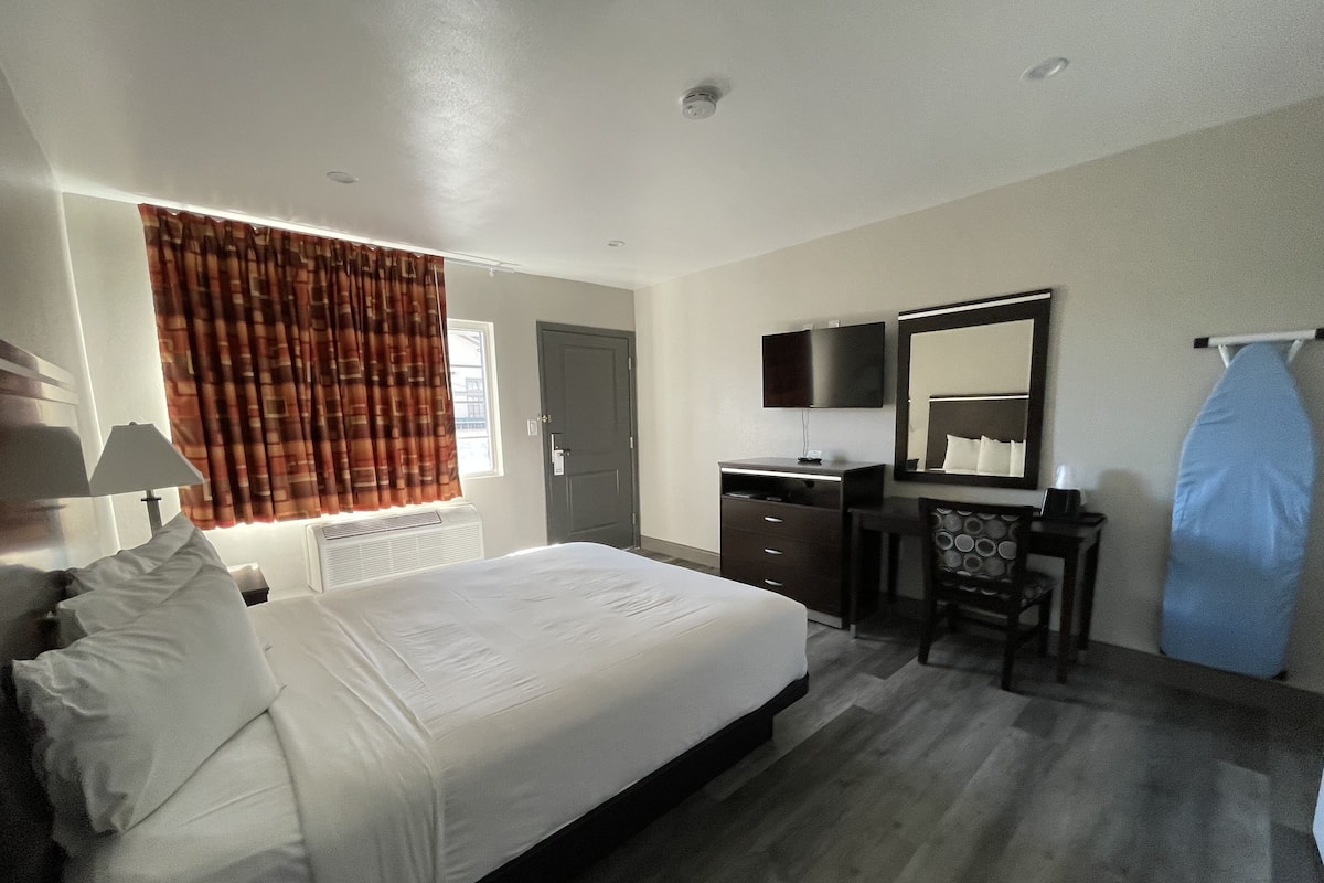 A hotel room with a bed, a desk, a chair, a mirror, and a window with curtains.