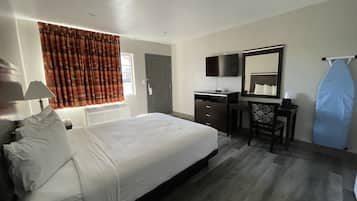 Habitación de hotel con cama, escritorio, silla, espejo y ventana con cortinas.