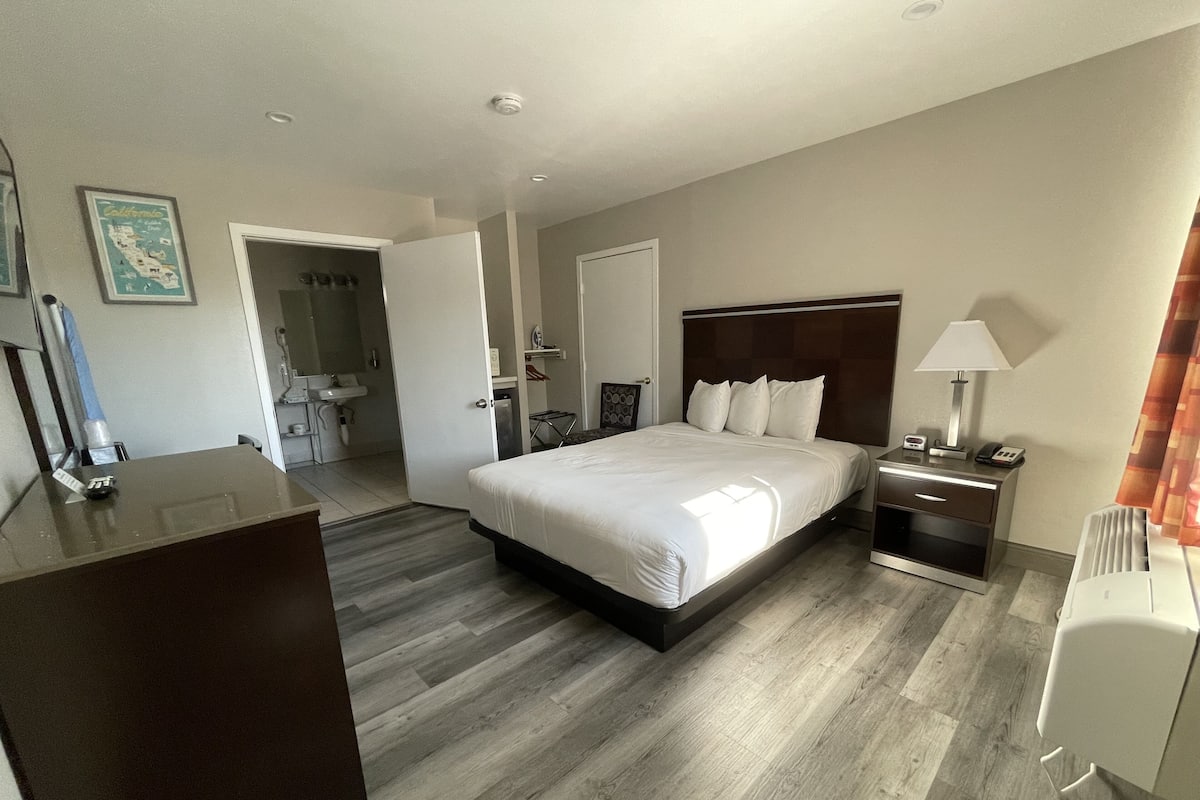 A hotel room with a large bed, bedside tables, a desk, a mirror, and a bathroom visible through an open door.
